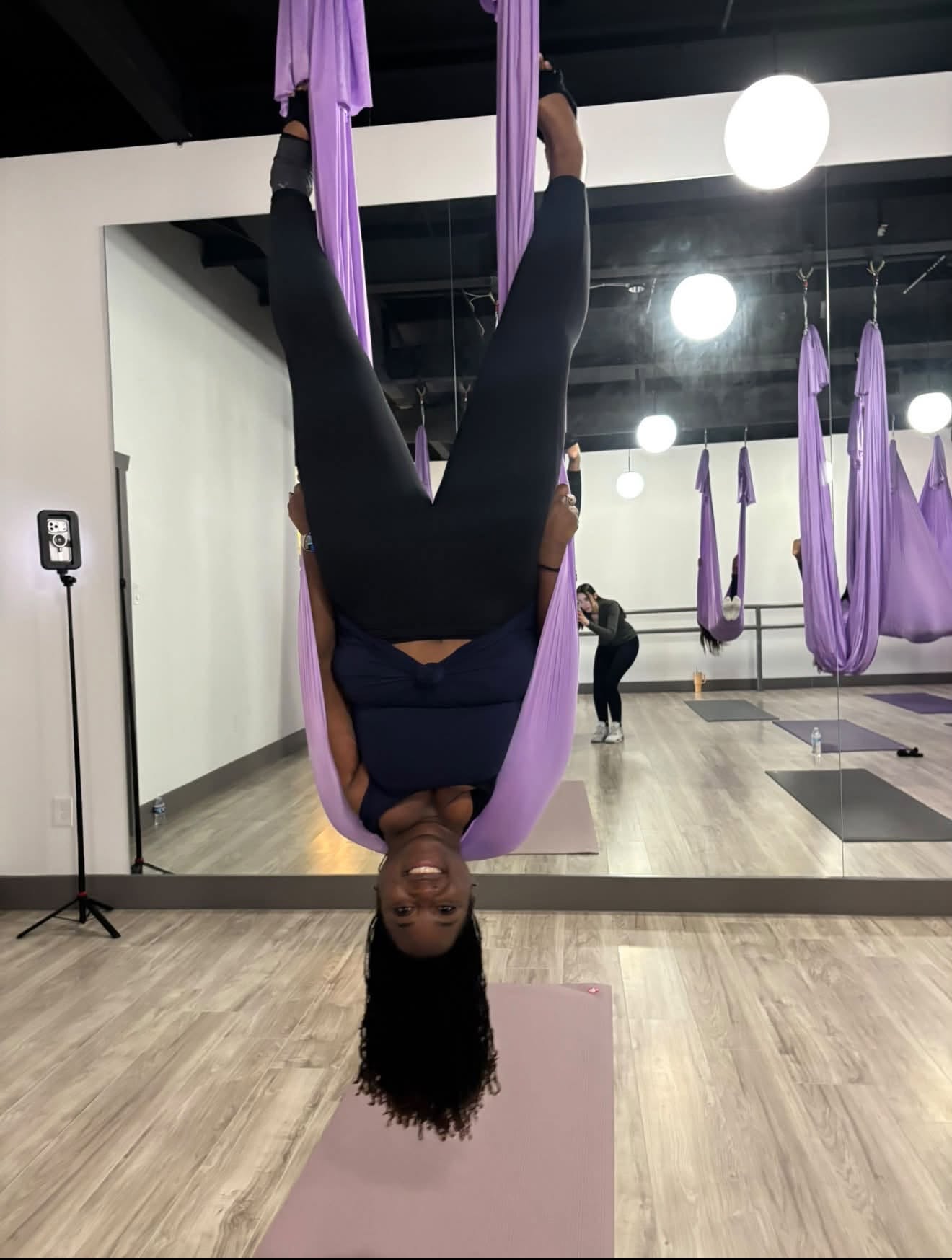 Quisha practicing an inverted aerial yoga pose in purple silks